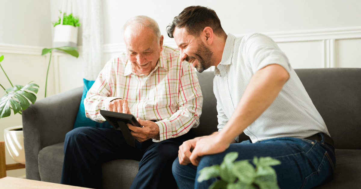 Senior man scrolling through tablet with adult son sitting on couch