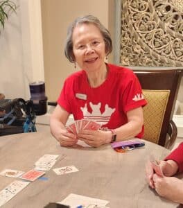 Resident Sylvia sits at a table, smiling with hand of cards