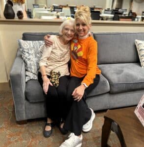 Two women sit smiling in an embrace on a sofa 