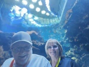 An older man and woman smile in front of an aquarium with brightly-colored fish