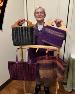 A woman in glasses holds up two woven purses with wooden handles. Two more woven bags are displayed below. 