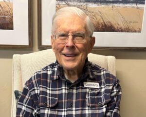 Older man in plaid shirt and glasses seated smiling for camera